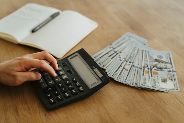 person using a calculator with cash and notebook next to them